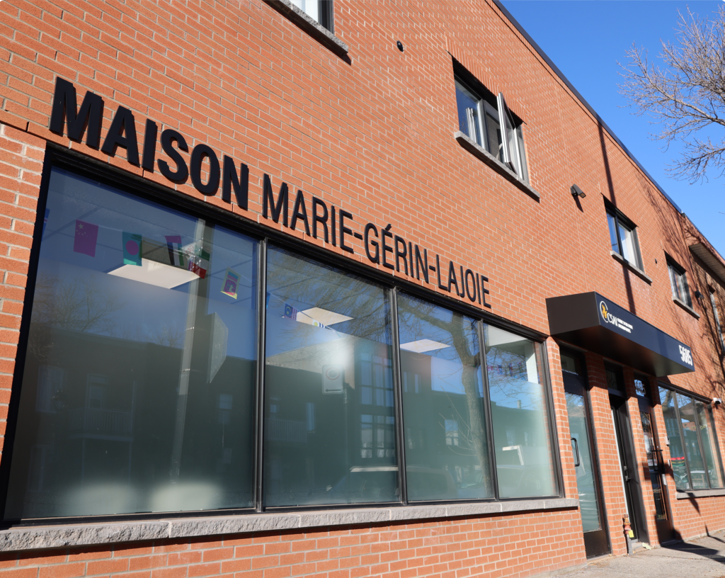 Façade de La Maison Marie-Gérin-Lajoie, un bâtiment en brique rouge avec de grandes fenêtres et une enseigne en lettres noires. Ce centre d’hébergement temporaire, géré par le CSAI, accueille les réfugiés pris en charge par l’État (RPCÉ) à Montréal.